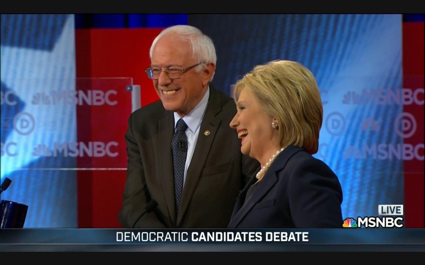 Bernie Sanders and Hillary Clinton shake hands and smile